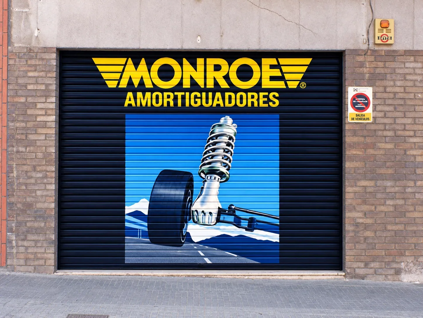 Persiana metálica decorada con pintura publicitaria de MONROE Amortiguadores por Àbac Rètols.